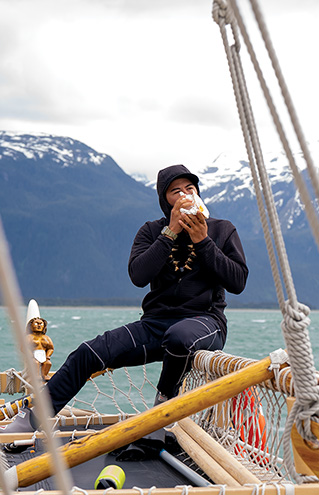 a person sitting on a boat blowing on a shell