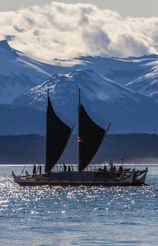 a boat with a large sail on water with mountains in the background