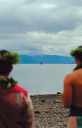 a group of people sitting on a beach looking at a sailboat