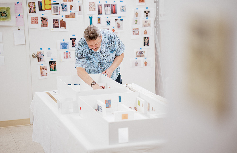 a person working on a miniature set featuring the layout of an exhibit