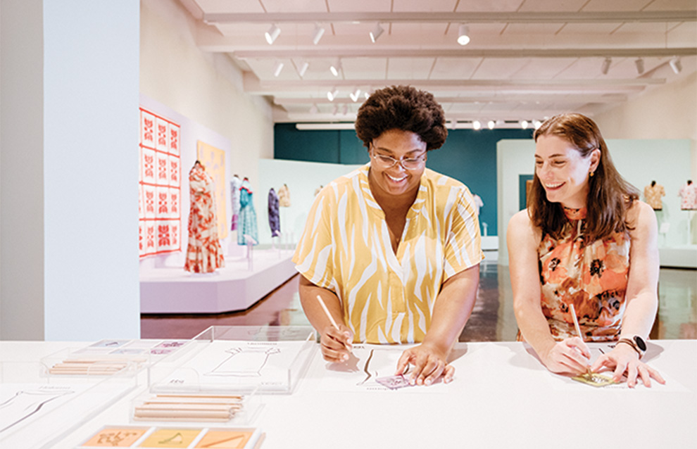 two people working on a table with clothing displayed on the back