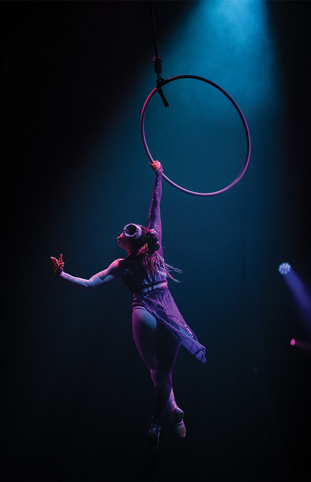 a person hanging on a suspended hula hoop with dramatic lighting